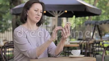 老女人坐在户外咖啡厅，在智能手机上因失物招领
